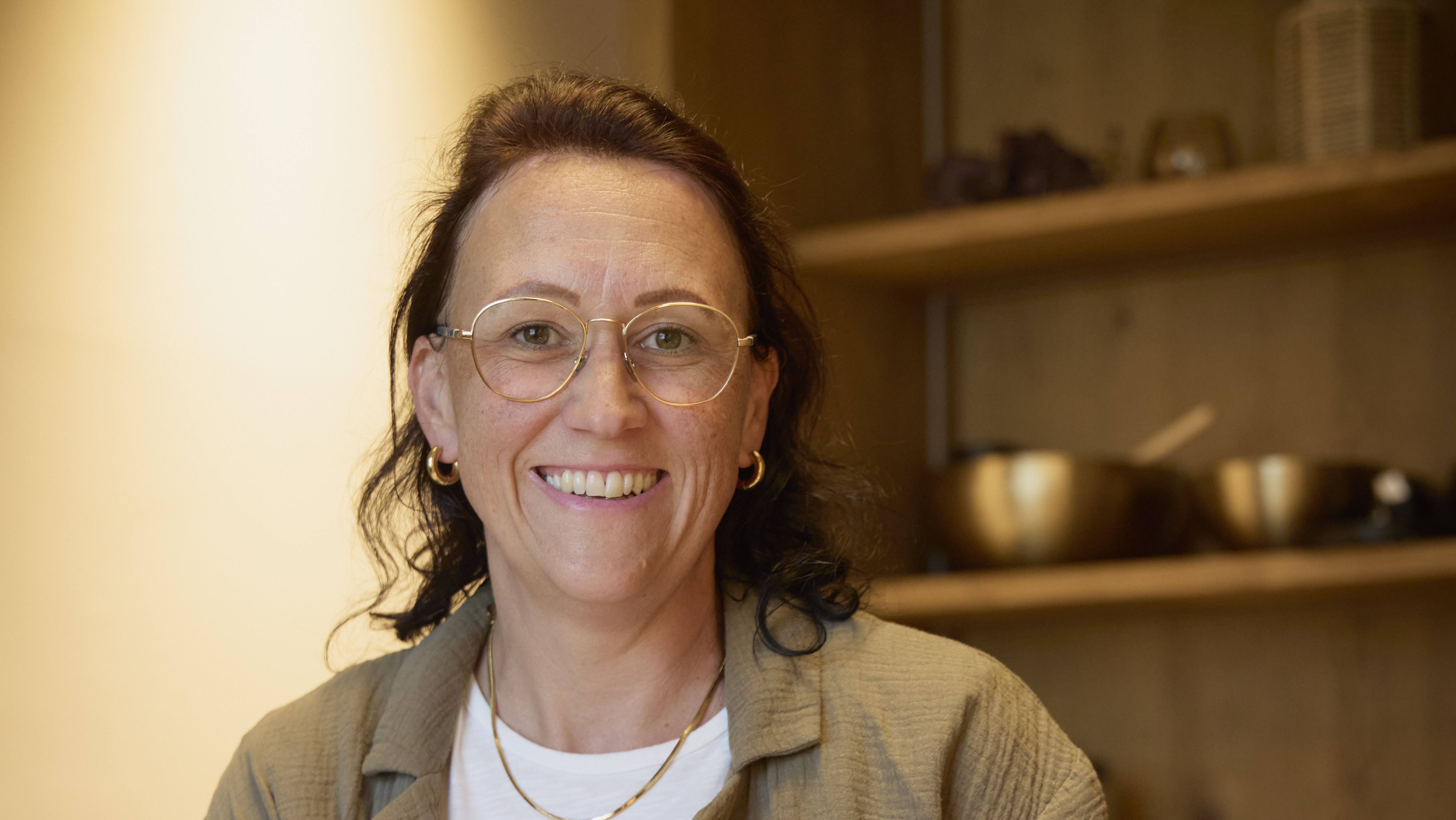 Frau in lässiger Kleidung sitzt in einem Therapieumfeld mit therapeutischen Werkzeugen im Hintergrund.