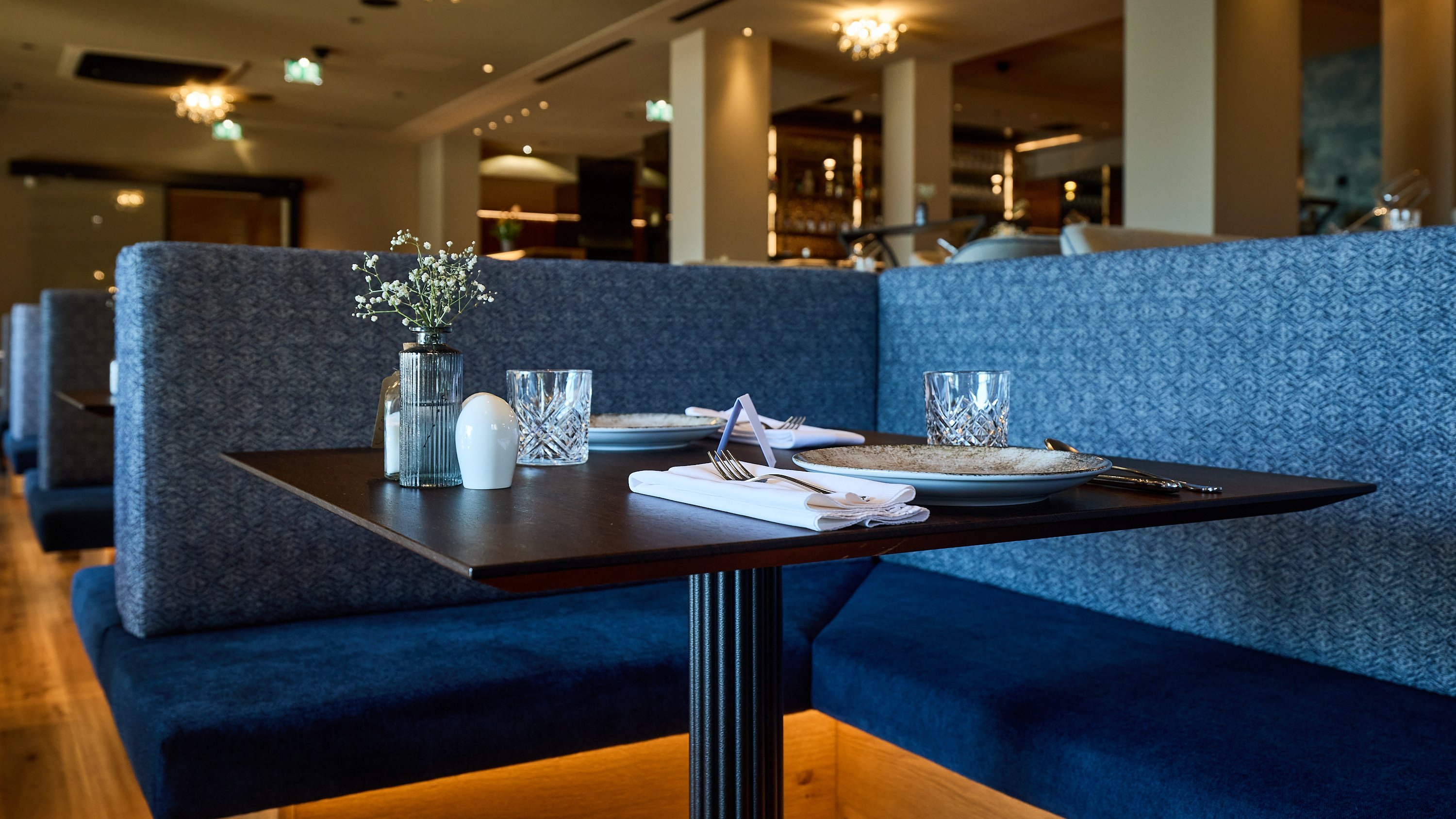 Modernes Restaurantdesign mit Stil Eleganter Esstisch im modernen Restaurant mit Gläsern und Besteck, umgeben von gepolsterten Sitzgelegenheiten.