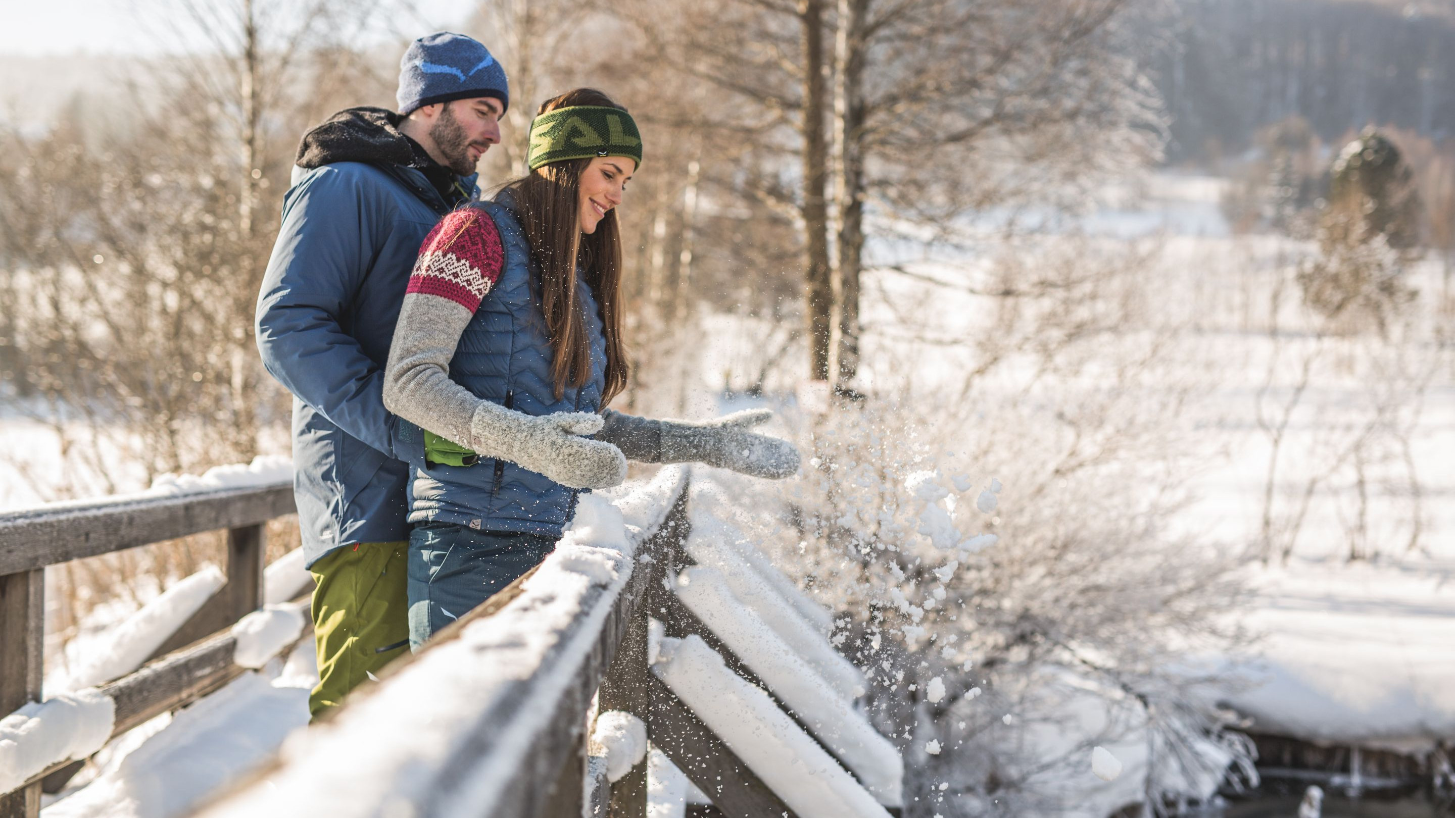 Couple enjoying snowy landscape on a wooden bridge, throwing snow