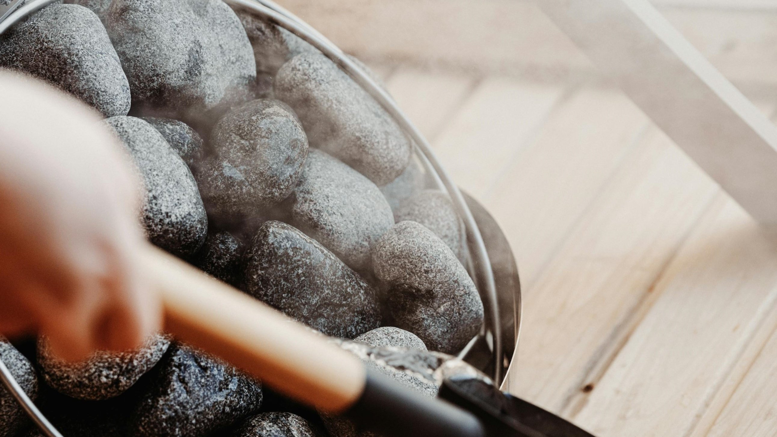 Hand holding a tool over hot stones for sauna infusion at Vogl's Nest.