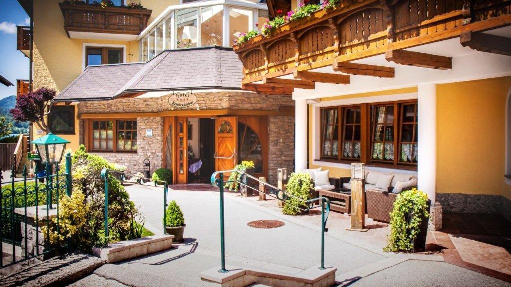 Außenansicht eines Hotels mit Stein- und Holzarchitektur, umgeben von Landschaft und Sitzbereichen