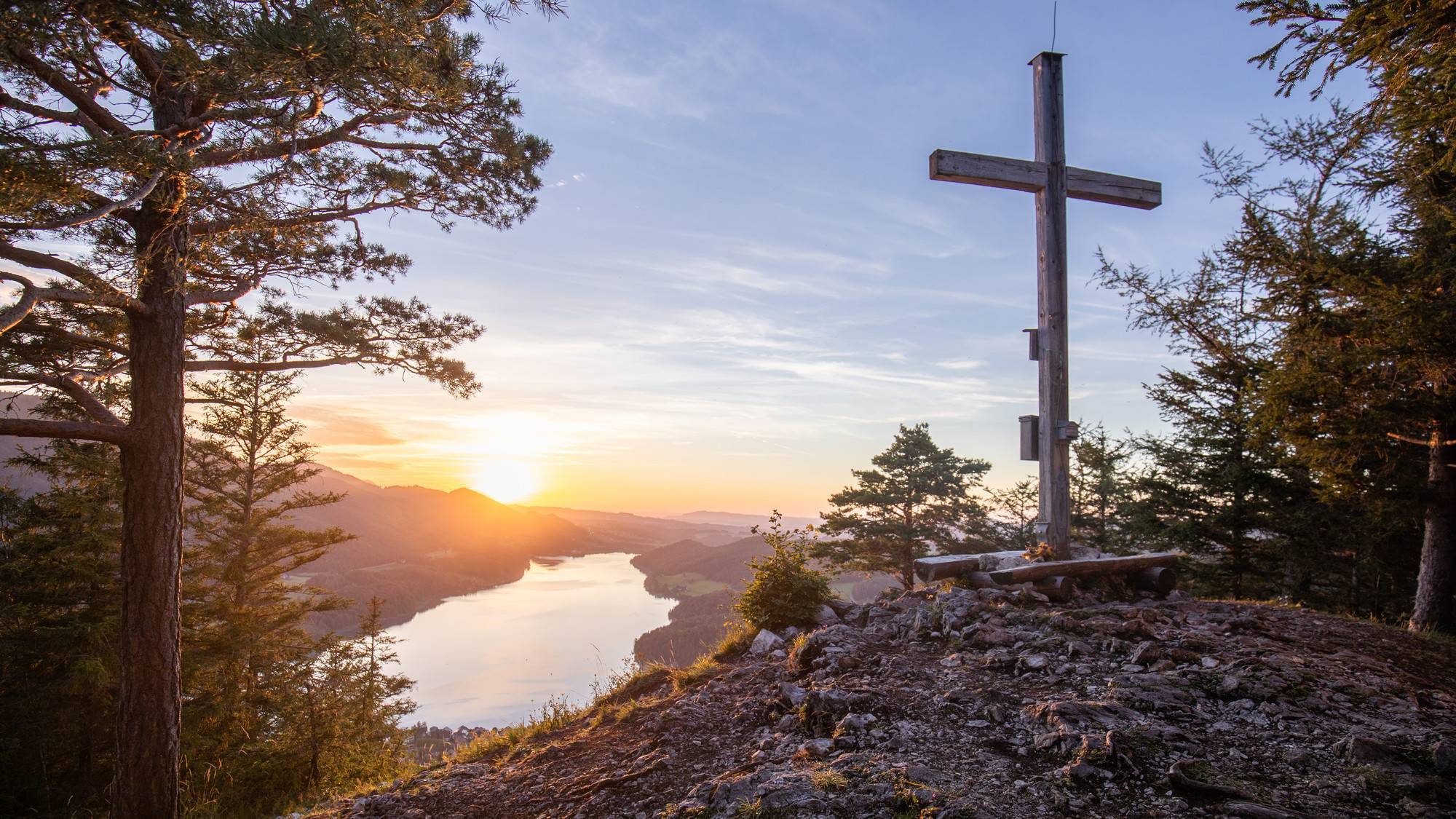 Scenic Sonnenuntergang Blick über den See mit hölzernen Kreuz Heitere Sonnenuntergangslandschaft über einem See mit Bäumen und einem Holzkreuz