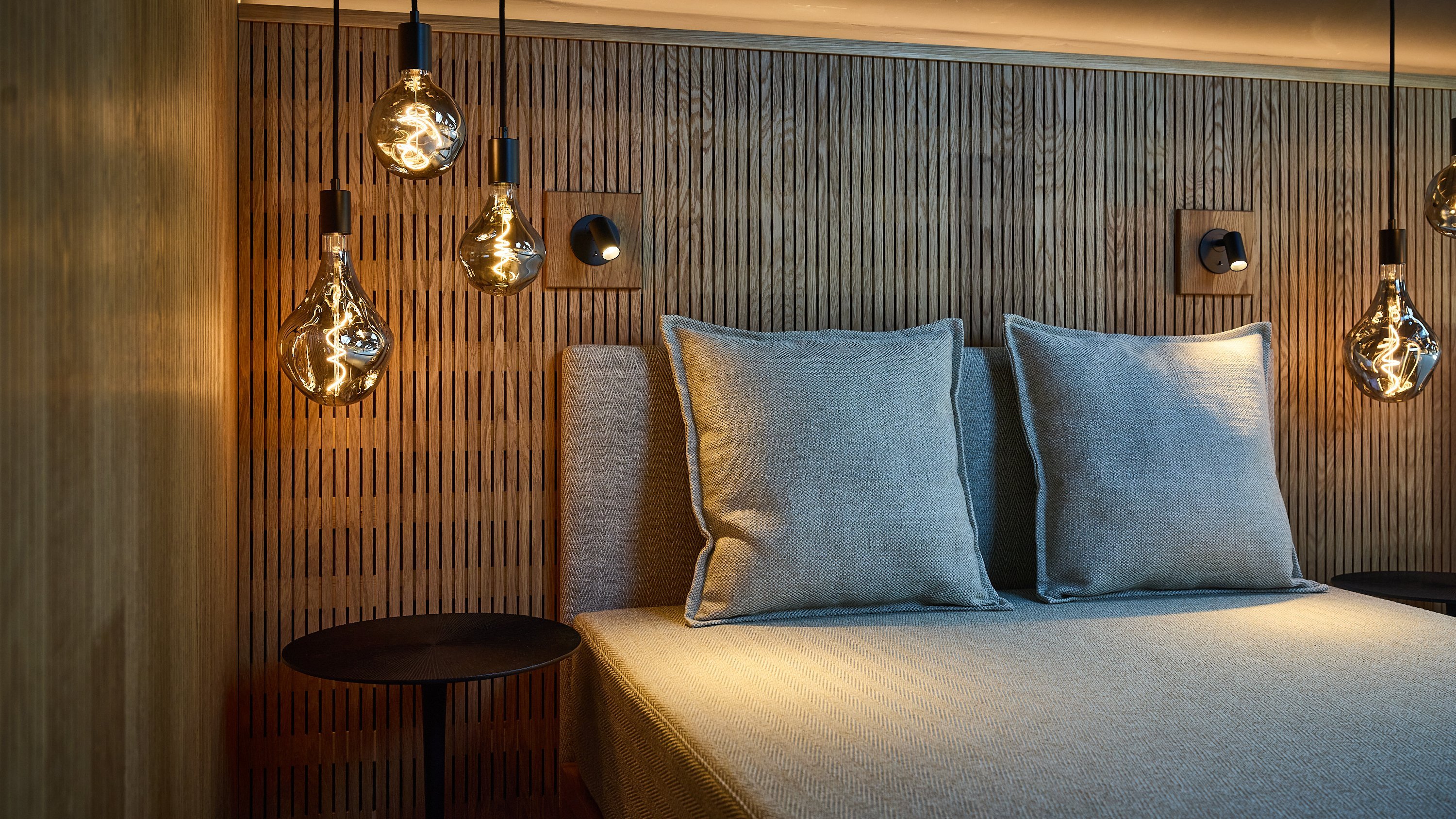 Schlafzimmer mit Bett, zwei Kissen und hängenden Lampen an einer Holzwand im minimalistischen Stil