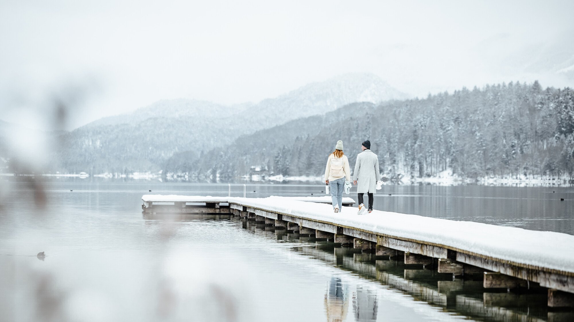 Paar zu Fuß auf verschneiten Pier von ruhigen See in Winterlandschaft